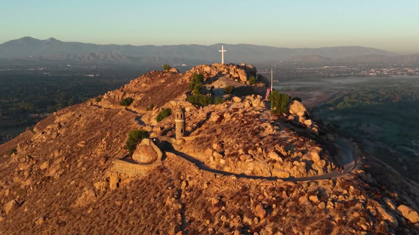 Aerial view of rocky summit with cross, peace tower, and flag at sunrise or sunset