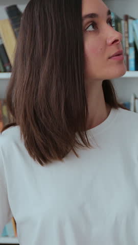 Caucasian girl in white t-shirt walks along the shelves with books in the library. University library concept.
