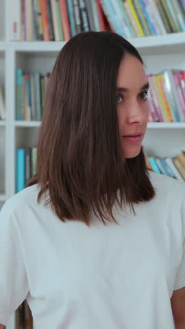 Caucasian girl in white t-shirt walks along the shelves with books in the library. University library concept.