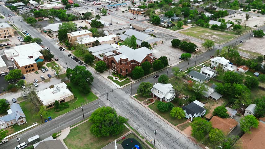 Drone view of a red brick church surrounded by downtown streets, homes and leafy neighborhoods in Kerrville Texas