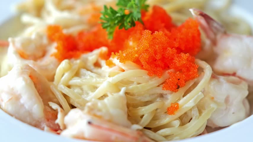 Creamy carbonara spaghetti topped with succulent shrimp and vibrant salmon roe, combining rich pasta sauce with delicate seafood flavors in an elegant dish.