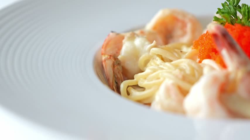 Creamy carbonara spaghetti topped with succulent shrimp and vibrant salmon roe, combining rich pasta sauce with delicate seafood flavors in an elegant dish.