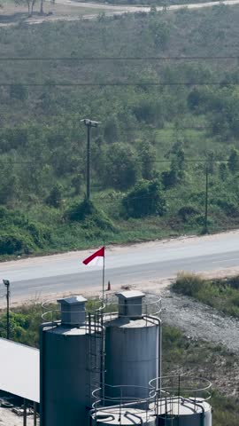 Indonesian flag fluttering atop industrial silos located by a quiet road in South Kalimantan