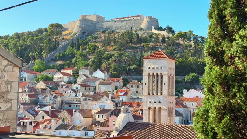Fortress on a hill overlooking a coastal town with traditional architecture and greenery in the foreground in Hvar, Croatia 