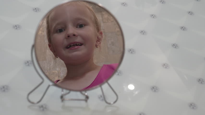 Reflection of a cute little girl looking in a round mirror, close-up shot, Little girl looking at her face reflection in a small vanity mirror