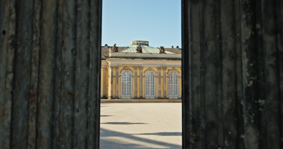 View through a gateway toward Sanssouci Palace in Potsdam, Germany, with arched windows across the courtyard facade.