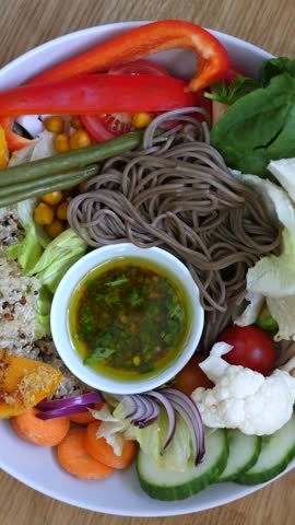Vegetarian salad plate rests on wood, styled in vibrant gourmet arrangement with soba noodles, fresh vegetables, and herb sauce. Colorful vegetarian salad plate looks fresh and inviting.
