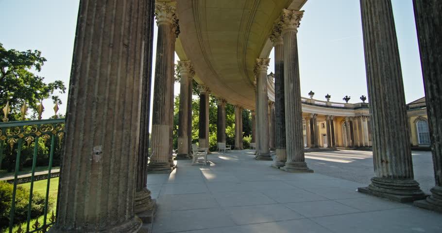 Fluted columns along the curved colonnade of Sanssouci Palace in Potsdam, Germany, with benches beside the walkway.