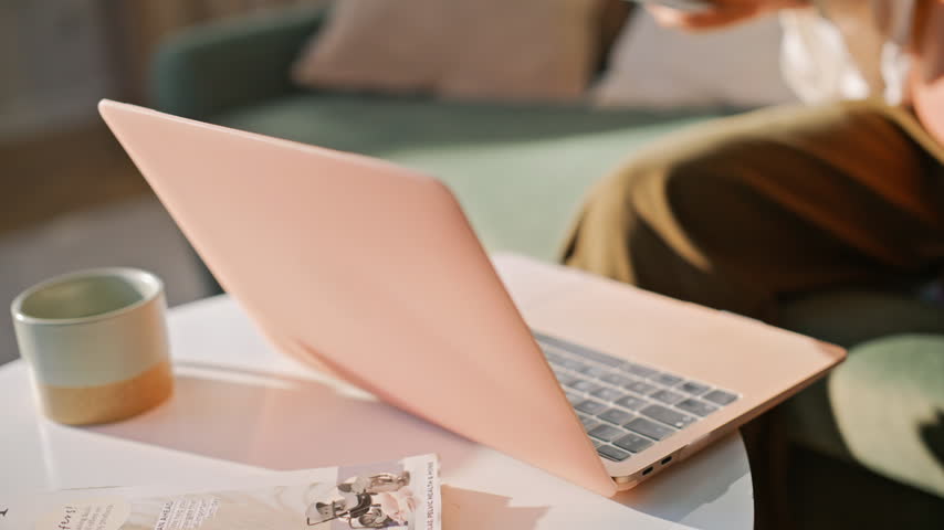 Woman examining ultrasound sonogram photo sitting sofa home. Closeup pregnant belly hands holding baby scan, thoughtful expectant lady, laptop nearby, cozy maternity moment living room indoors.