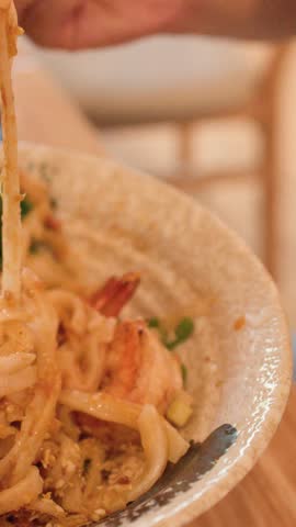 Close-up of hands using chopsticks to lift noodles from a prawn bowl in Bangkok.