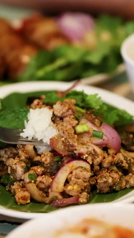 Close-up of a fork lifting spicy minced pork salad and sticky rice in Bangkok, Thailand.