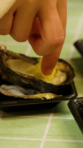 Close-up of a hand squeezing lemon over a fresh raw oyster in Tokyo, Japan.