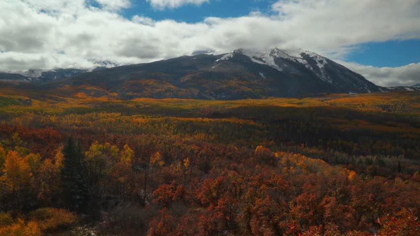 Aerial View of Colorful Autumn Forest Valley Below Snow Capped Mountain Peak