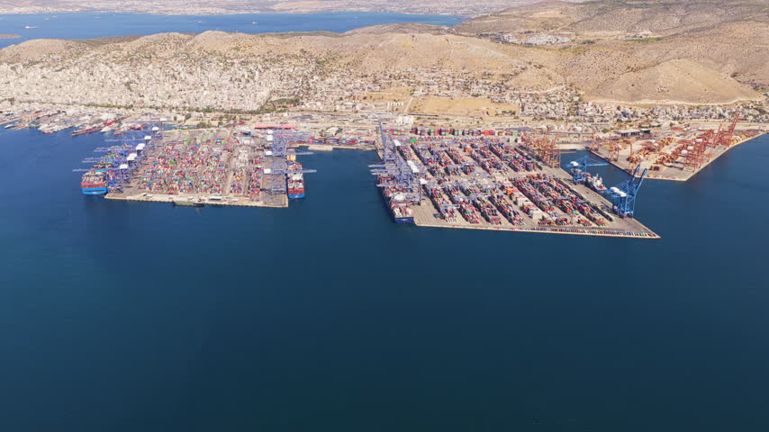 Aerial perspective of the Port of Piraeus, the largest port in Greece, with container ships being loaded and unloaded by large gantry cranes at the commercial cargo shipping terminal