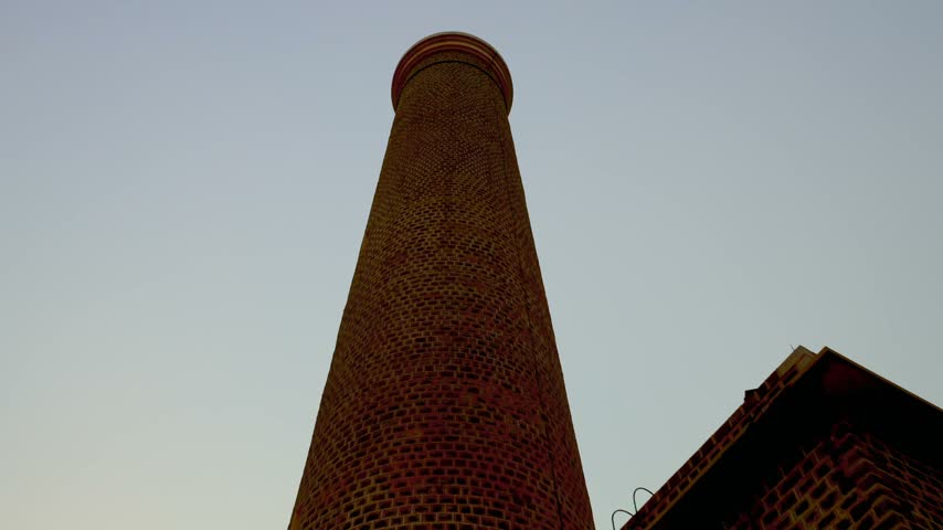 Low angle view looking up at the tall brick structure of Sanganeb lighthouse against a clear sunset sky in Sudan