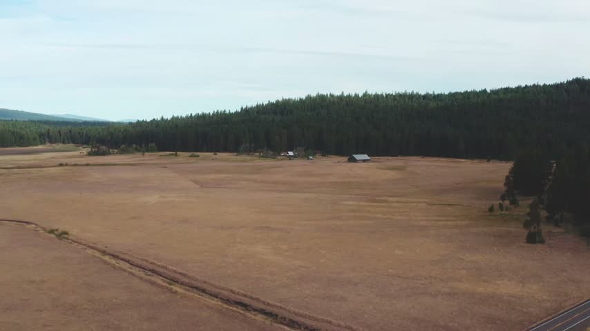 Drone view of farmland and barns below forested Cascade Range foothills