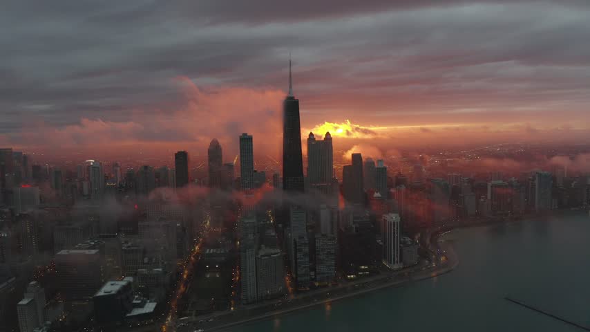 Breathtaking aerial footage of Chicago skyline during sunrise showcasing skyscrapers piercing through low hanging clouds over Lake Michigan captured with cinematic motion and vibrant warm lighting.