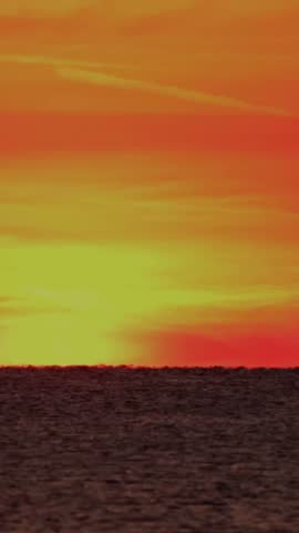 This time-lapse shows the sun setting over the ocean. The sun moves down and changes color from bright yellow to deep orange. The sky transitions through various shades as the light fades.