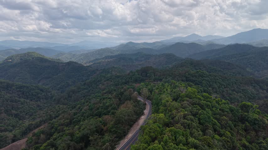 Tranquil aerial view of a winding road through highland terrain with distant blue mountain layers.