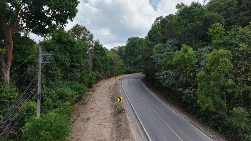 Scenic aerial shot of a paved road bending around a forested mountain with misty ranges beyond.