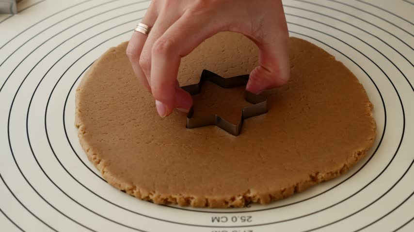 Woman cutting star shaped gingerbread cookie from rolled dough for Christmas baking.