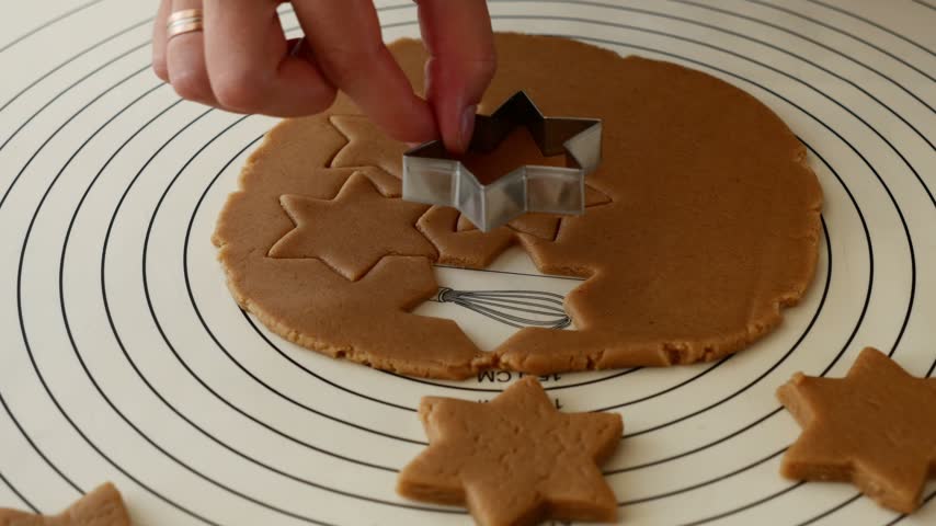Woman cutting and lifting star shaped gingerbread cookie from dough for Christmas Baking