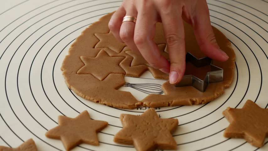 Close-up of woman cutting star shaped gingerbread cookies from dough for Christmas baking.