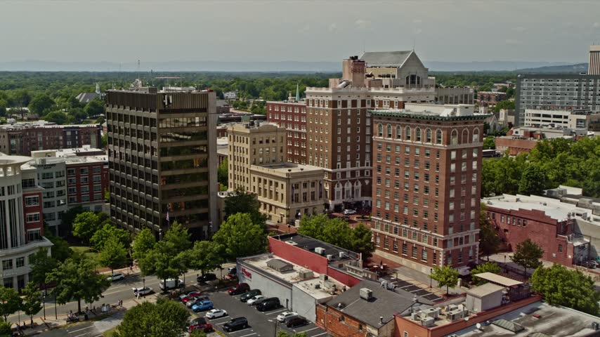 High angle drone shot captures cityscape of Huntsville Alabama featuring landmark historic hotels office complexes multistory parking garages and elevated highway traffic flowing through city center.