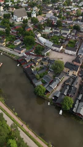 Vertical screen aerial drone view of Porvoo Finland showing bright historic houses red warehouses along the river and colorful waterfront architecture under clear daylight