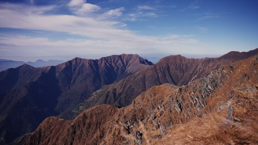 A jagged rocky ridgeline gives way to a forested valley and winding trail far below.