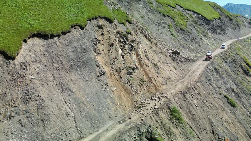 Aerial drone footage showing loose rocks falling onto a dirt road from a steep rocky mountain slope. Datvisjvari Pass, Georgia.