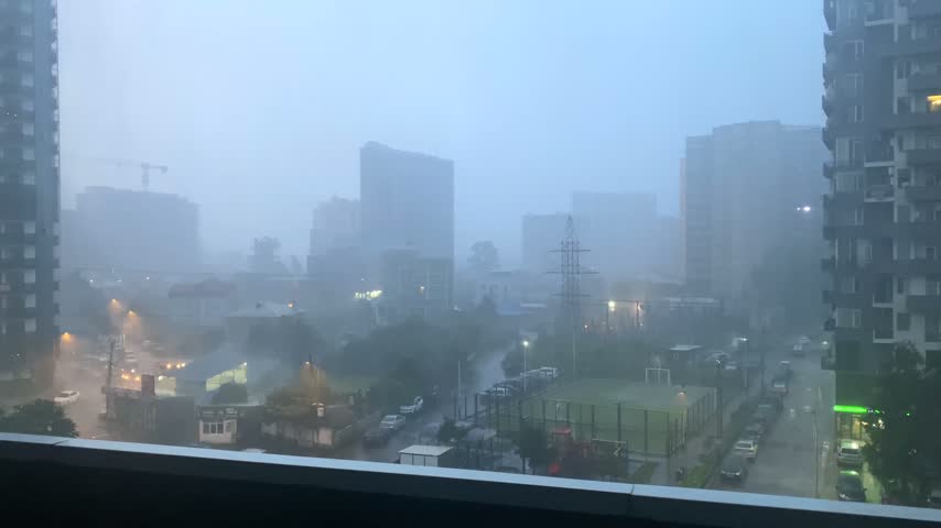 Rain falling over Batumi high-rise district in elevated city view, reducing visibility across streets and towers, suited for weather reporting, urban climate coverage, rainy season travel information