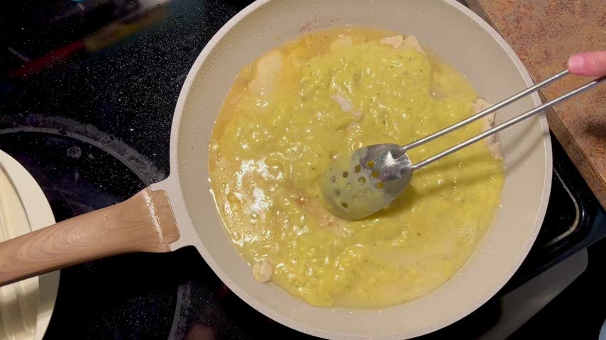 Spoon stirring creamy sauce and chicken simmering in a frying pan on a stovetop