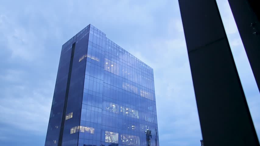 A reflective glass office tower showing a faint statue reflection against an overcast rainy sky in Mexico City.