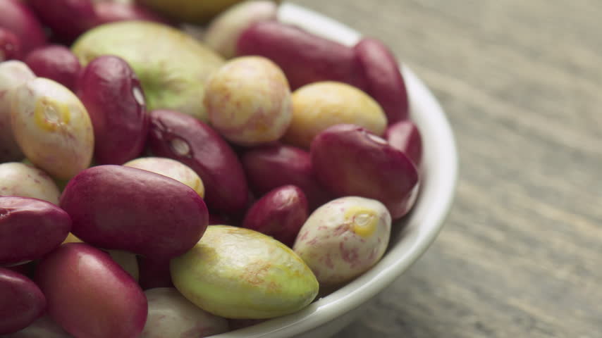 Fresh beans of different varieties and sizes on white plate. Macro shot. Colorful beans on wooden table. Product of organic farming. Healthy eco vegetarian food.