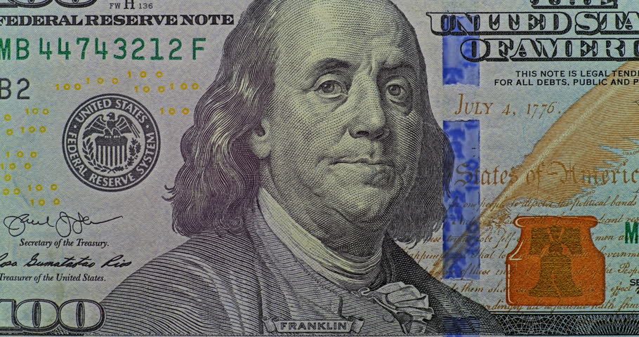 Real footage of US hundred dollar bills. Real footage of US one hundred dollar notes features Benjamin Franklin portraits and shifting golden reflections. This currency detail holds steady while light glides across printed security elements.