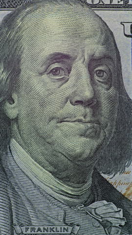 Benjamin Franklin dollar bill close up. Benjamin Franklin on dollar bill appears in real camera recording. Close up view holds on printed currency as changing light reveals paper texture, engraving lines, and familiar portrait.