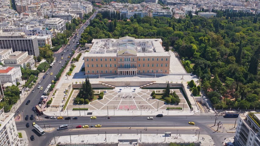 High-angle drone footage capturing the iconic Hellenic Parliament building, Syntagma Square, and the surrounding city traffic on a sunny day in Athens, the historic capital city of Greece
