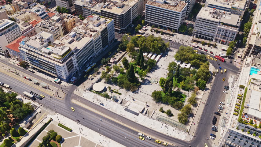 High-angle aerial view capturing the urban landscape of Klafthmonos square, showing the bustling city life with traffic moving through the streets of Athens and buildings surrounding the green park