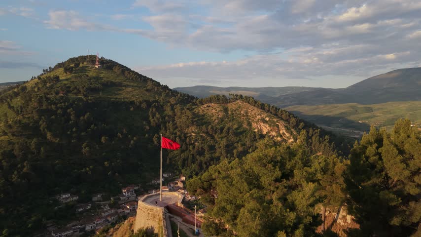 Aerial view of the historic stone walls of Berat Castle at sunset with a red flag flying in the breeze in Berat, Berat County, Albania.