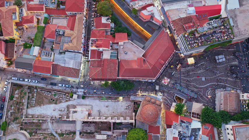 Dramatic aerial top-down view rotating over the historic Monastiraki Square in Athens, revealing ancient ruins, bustling crowds, rooftop restaurants, and city traffic at dusk