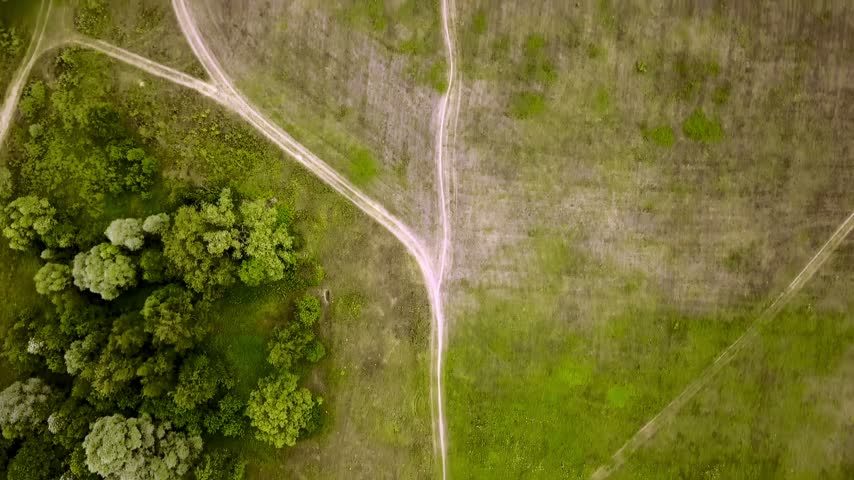 Aerial top down view of dirt country roads curving through green grass fields in summer countryside