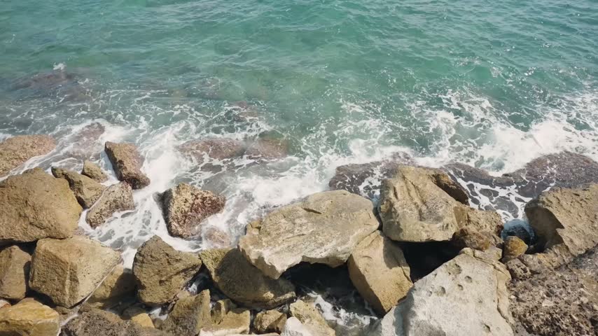 Ocean Waves Crashing Against Large Shoreline Rocks In Turquoise Water Top View