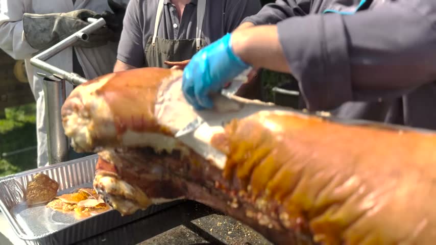 Close-up video footage of a chef carving a deliciously roasted pig with crispy skin during an outdoor barbecue event, highlighting culinary preparation.
