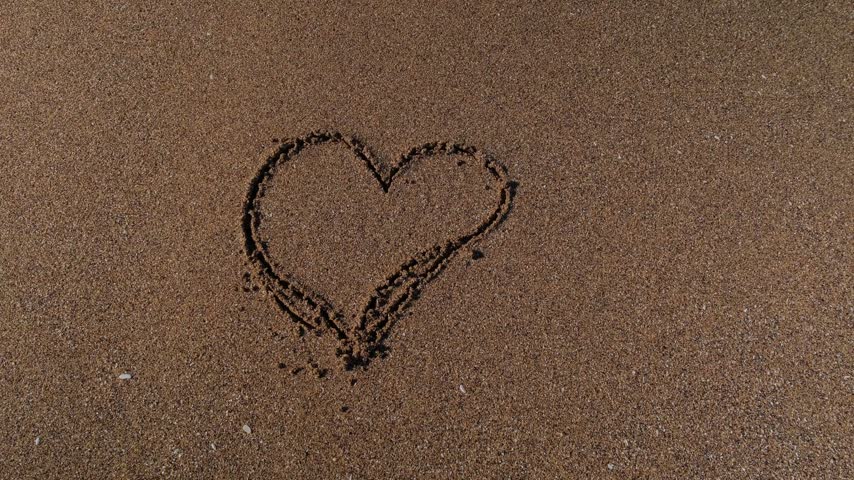 Heart drawn in the sand is washed away by the sea waves