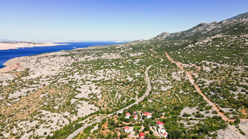 Aerial view of cars drives along a winding road through rocky mountains near small village in Croatia. Summer road trip through the wild landscape of the Adriatic coast.