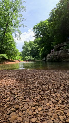 Vertical clip of the scenic rock formations and natural swimming hole at Bell Smith Springs in Shawnee National Forest. Captures distant park visitors swimming and jumping off cliffs into the water.