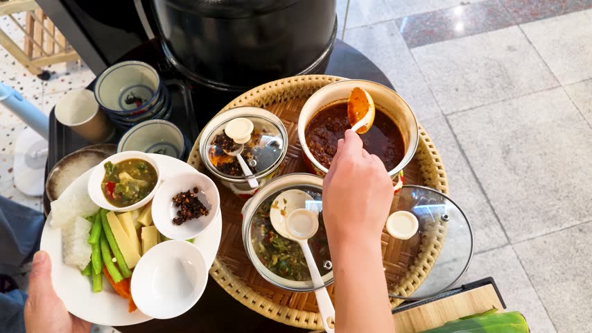 High-angle view of hands serving spicy chili dip onto a fresh vegetable platter.