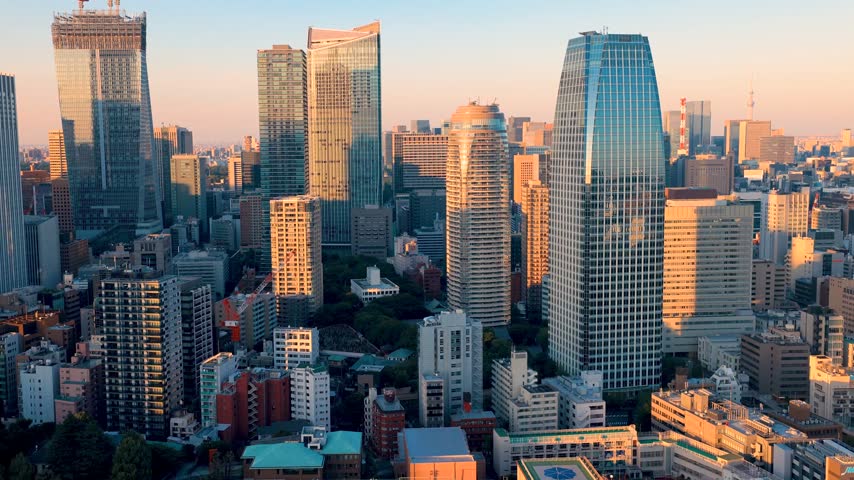 Aerial view of a sprawling metropolitan skyline during a golden hour sunset featuring modern office towers and active urban development in a dense downtown district