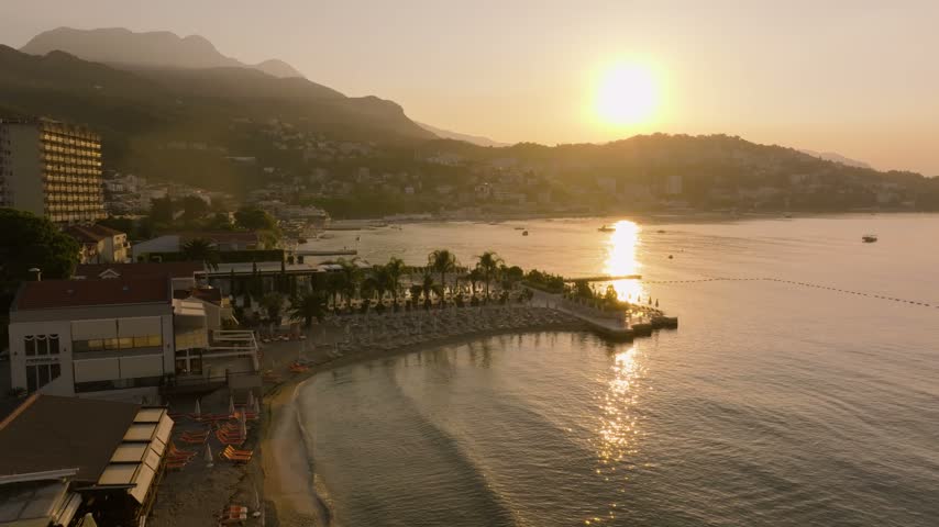Palm-lined resort pools, sun loungers and a curved swimming cove sit quiet at sunrise with the sun reflecting across the bay.